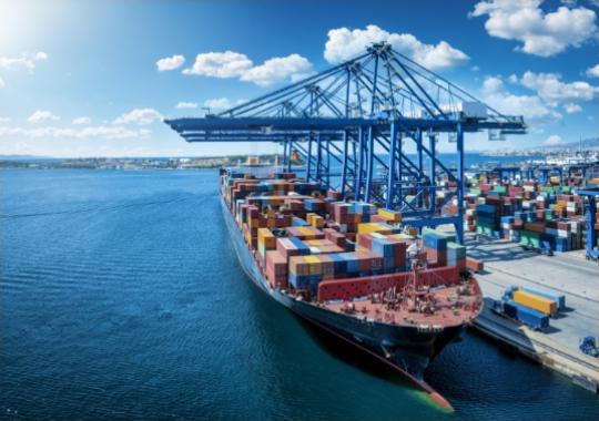 Nave cargo colma di container colorati, attraccata in porto sotto un cielo azzurro e sereno.